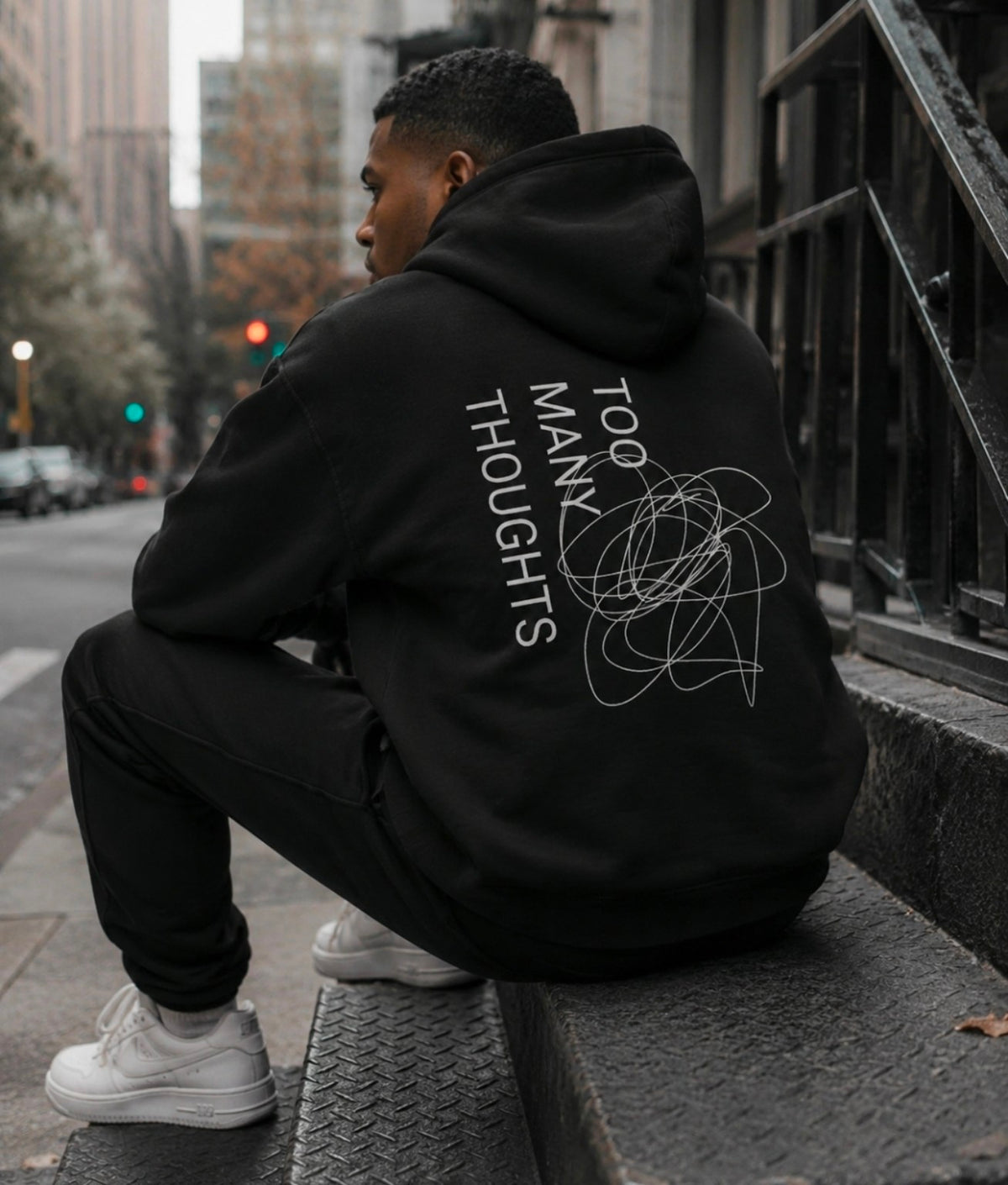 Model wearing a black Too Many Thoughts hoodie in a city setting