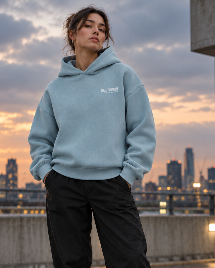 Model wearing the Pebble Sculpted Ultra-Heavy Hoodie with small white chest logo in an urban rooftop setting